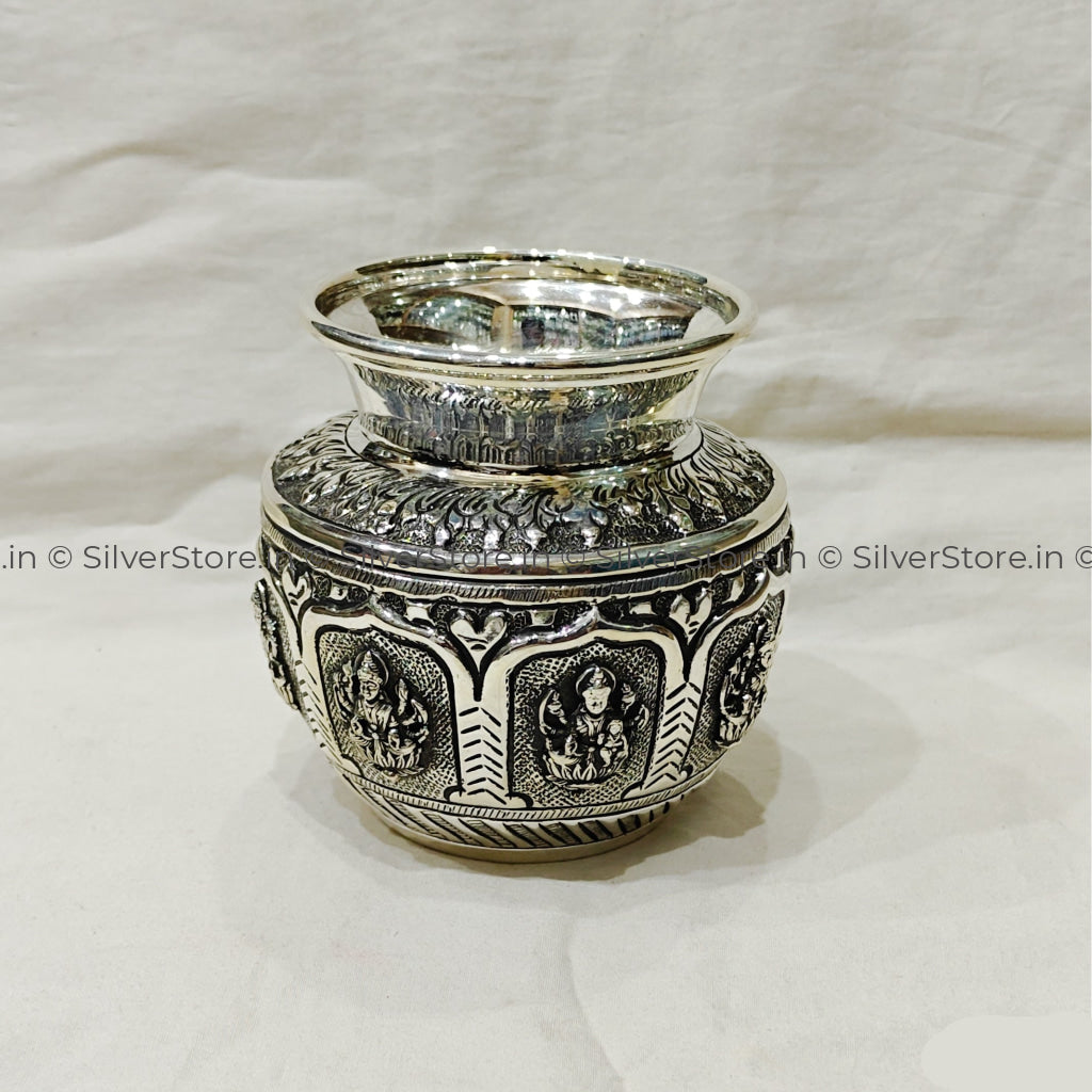 Decorative silver container with intricate designs on a white fabric background