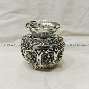 Decorative silver container with intricate designs on a white fabric background